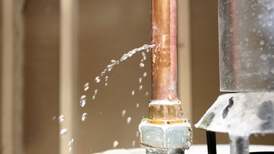 A copper pipe leaks on top of a water heater.